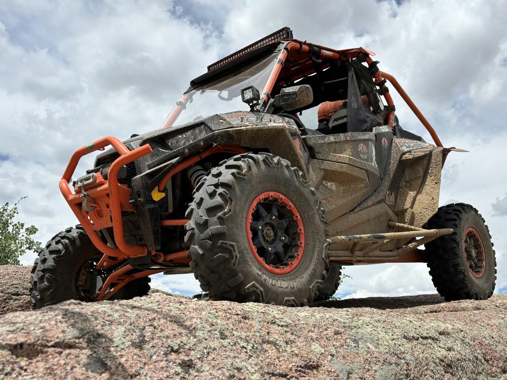 Mud-covered Polaris RZR side-by-side parked on a rock ledge